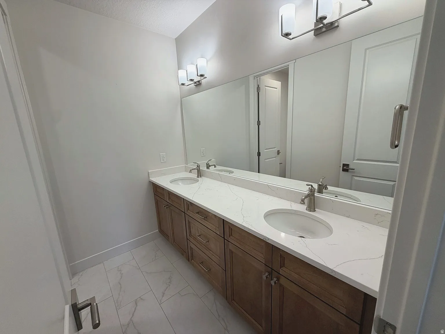Dual vanity with integrated sinks, white countertop, wood-finish cabinetry, and brushed nickel fixtures