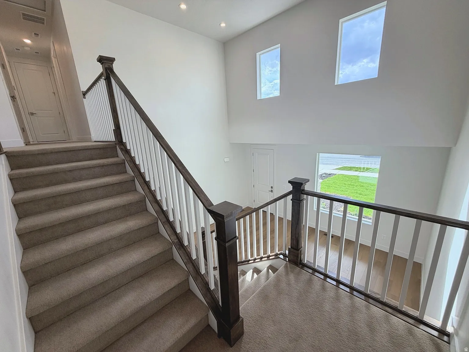 Multi-story interior featuring a carpeted staircase with wood and white baluster railing, high ceilings, recessed lighting, and multiple windows