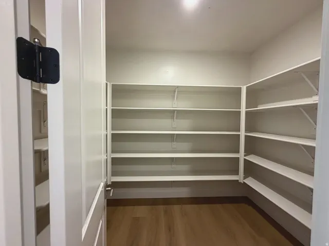 Expansive walk-in pantry with wrap-around white shelving, wood-finish flooring, and recessed lighting
