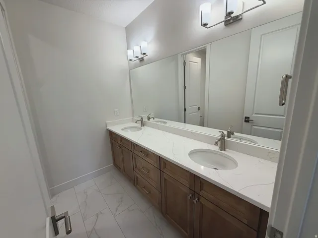 Dual vanity with integrated sinks, white countertop, wood-finish cabinetry, and brushed nickel fixtures
