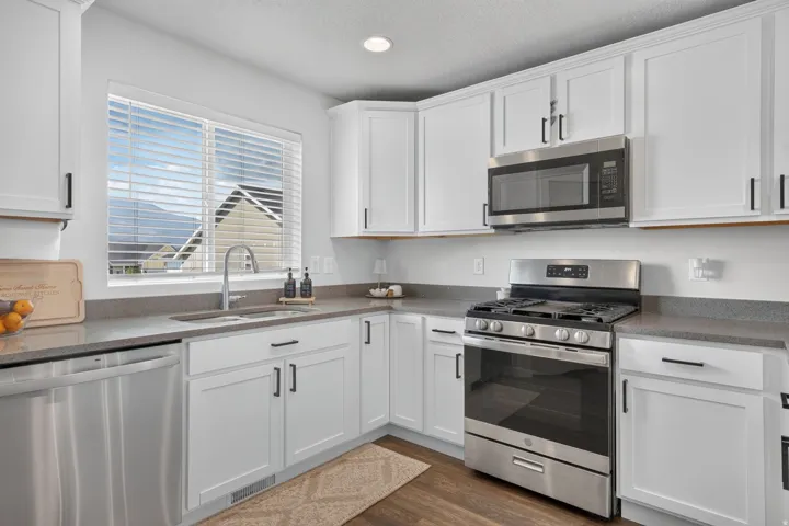 Kitchen featuring stainless steel appliances, white cabinetry, dark countertops, and wood-finish flooring