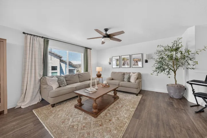 Spacious living area featuring wood-finish flooring, a ceiling fan, and a large window with blinds