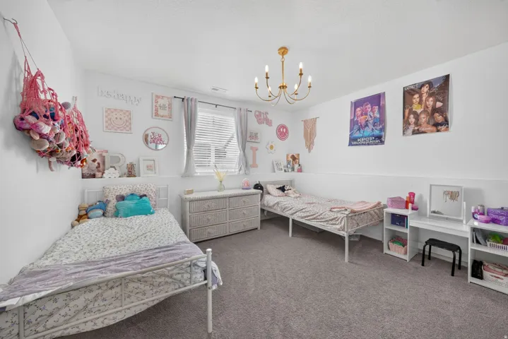 Wall-to-wall carpeting, window with blinds, and an overhead chandelier with candle-style lights