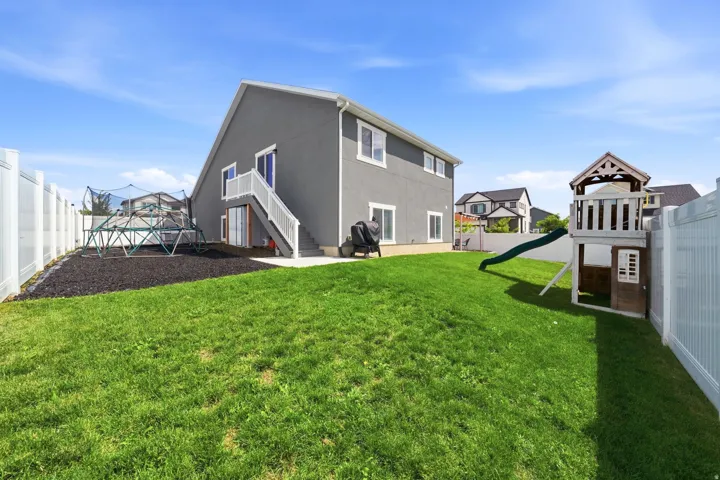 Rear exterior with gray stucco finish, white trim windows, white privacy fencing, and a manicured lawn