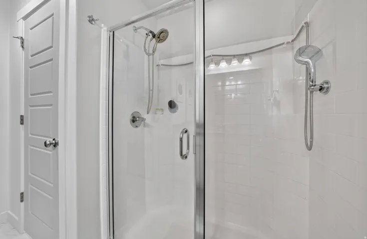 Glass-enclosed shower with subway tile surround, multiple shower heads, and chrome fixtures