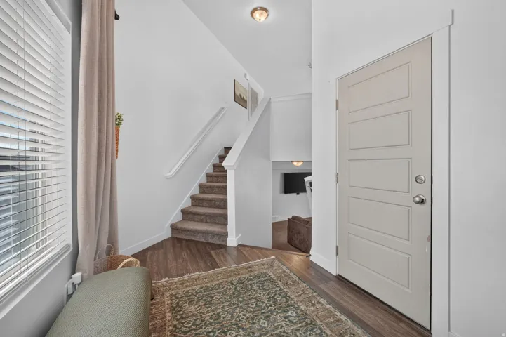Entryway featuring a panel door with brushed nickel hardware, wood-finish flooring, and a carpeted staircase with a white handrail