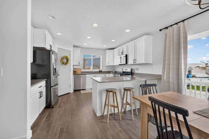 Kitchen featuring white cabinetry, stainless steel appliances, a center island with bar seating, and wood-finish flooring