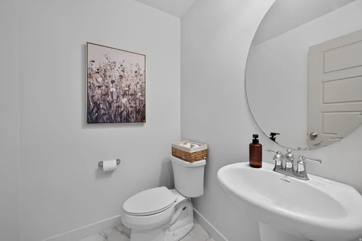 Pedestal sink with chrome faucet, circular frameless mirror, and white toilet