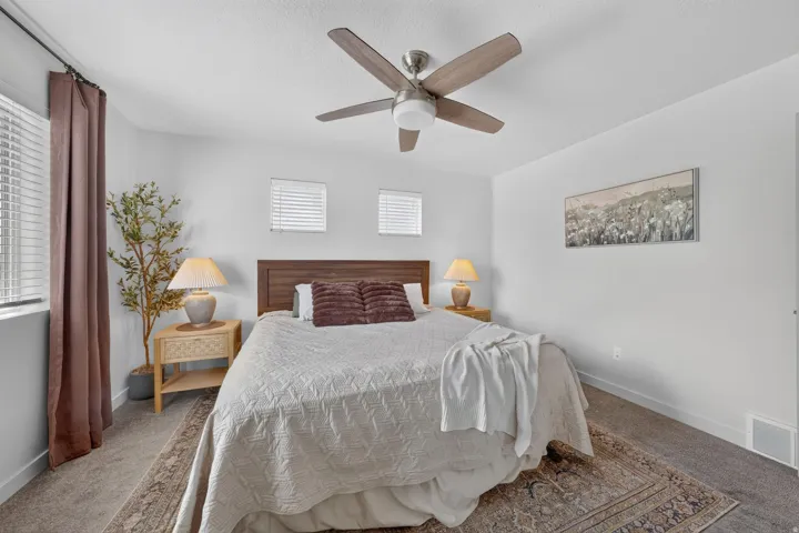 Carpeted flooring, wood-finish headboard, ceiling fan with integrated lighting, window blinds, and white walls