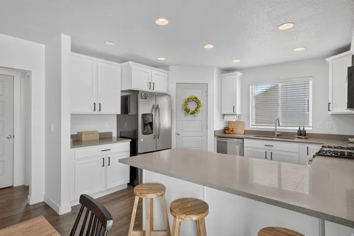 Modern kitchen featuring white cabinetry, a large center island with a light-toned countertop, stainless steel appliances, and wood-finish flooring