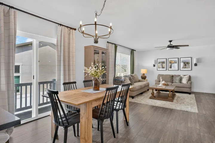 Open-concept living space with wood-finish flooring, a contemporary chandelier, and a sliding glass door leading to a balcony
