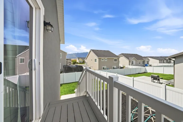 Sliding glass door access to an exterior balcony with composite decking and white railing, overlooking a fenced backyard with a grass lawn