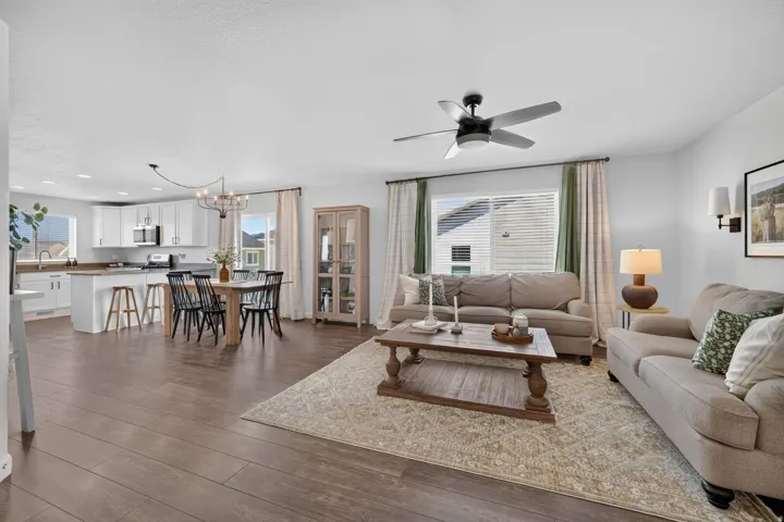 Open-concept living area featuring wood-finish flooring, white kitchen cabinetry, a kitchen island with seating, and a dining area with a chandelier
