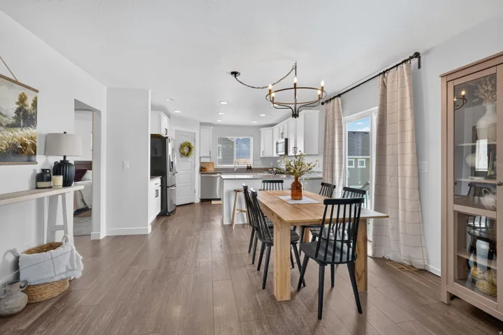 Open-concept dining and kitchen area featuring wood-finish flooring, a contemporary chandelier, white cabinetry, and stainless steel appliances