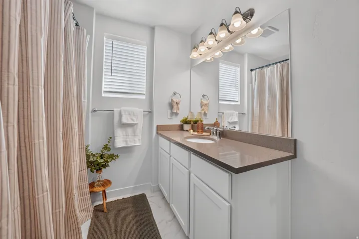 White cabinetry with brushed nickel hardware, expansive vanity with integrated sink, stone-finish countertop, and wall-mounted vanity lighting