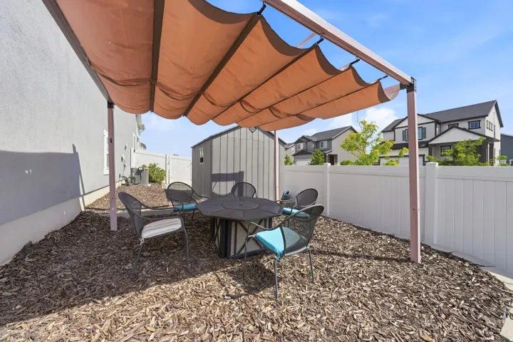 Outdoor patio with a retractable fabric shade structure, wood chip ground cover, and a white privacy fence