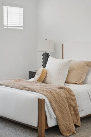White walls, a single window with blinds, wood-frame bed, and carpeting