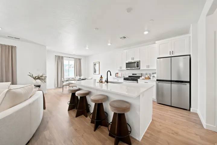 Open-concept living space featuring wood-finish flooring, a kitchen island with seating, white shaker cabinetry, stainless steel appliances, and recessed lighting