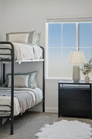 Carpeted bedroom with a window, metal-frame bunk beds, and a two-drawer nightstand