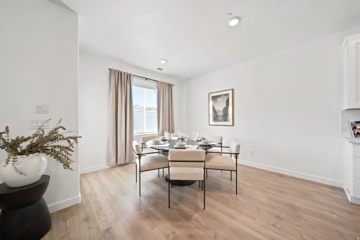 Bright dining area with wood-finish flooring, recessed ceiling lighting, and large windows dressed in neutral curtains