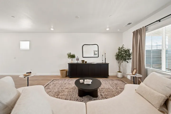 Recessed lighting, wood-finish flooring, white walls, and a large window with blinds and curtains