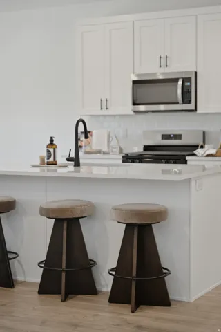 Kitchen island with a built-in sink, white cabinetry, stainless steel microwave, and gas range