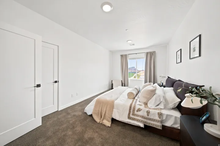 Spacious bedroom featuring neutral wall finishes, recessed ceiling lighting, carpeted flooring in warm tones, dual closets with white panel doors, and a large window with natural light and soft drapery