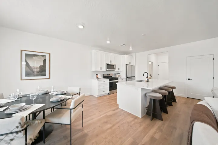 Open-concept living area with wood-finish flooring, white cabinetry, stainless steel appliances, and a kitchen island with seating
