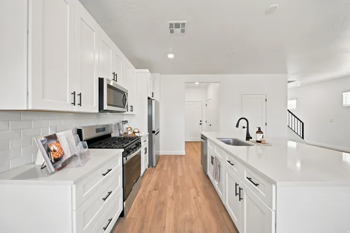White shaker cabinetry with matte black hardware, stainless steel appliances, subway tile backsplash, light wood-finish flooring, and white countertops