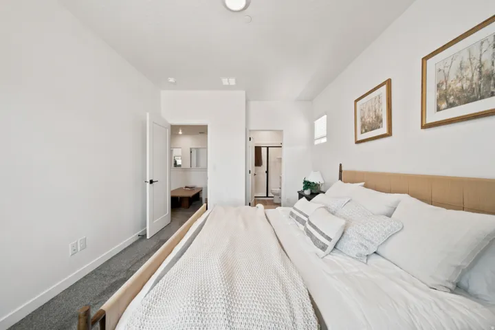 White walls, recessed ceiling lighting, light wood-finish headboard, white interior doors, and gray carpeting