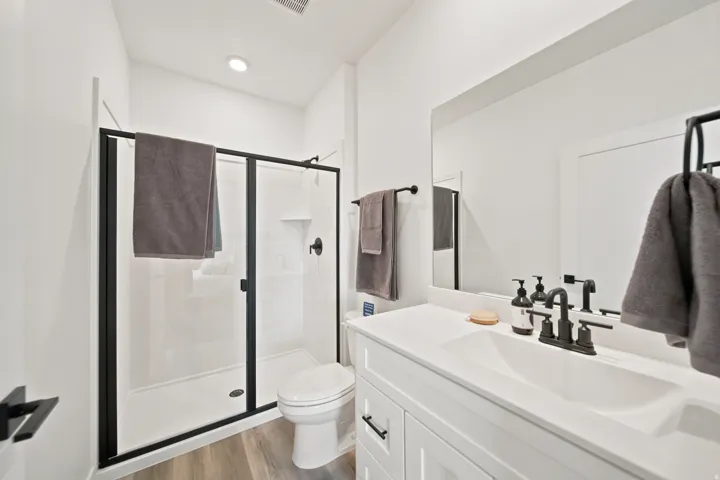 Contemporary bathroom featuring a black-framed glass shower enclosure, white vanity with integrated sink, matte black fixtures, and wood-finish flooring