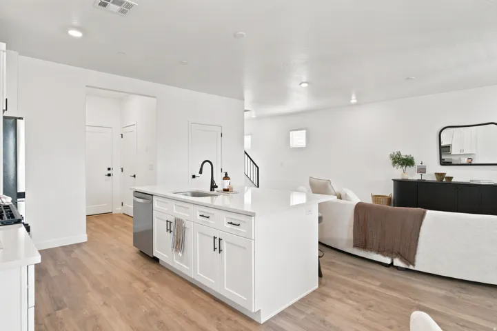 Kitchen island with white cabinetry, stainless steel dishwasher, and a black gooseneck faucet