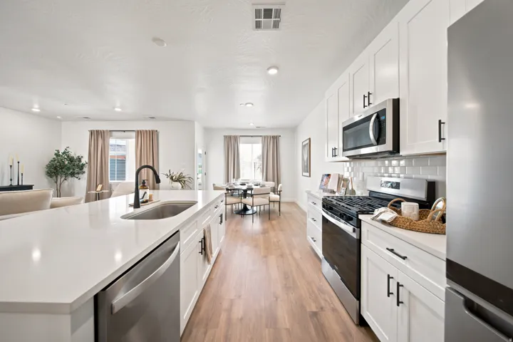 Open-concept kitchen featuring white cabinetry, stainless steel appliances, a large island with an undermount sink, and wood-finish flooring