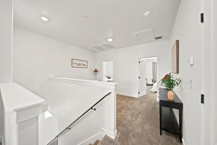 Carpeted hallway with white walls, black handrail, recessed lighting, and white trim