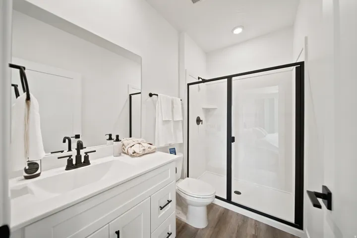 Bathroom featuring a white vanity with integrated sink, black fixtures, wood-finish flooring, and a glass-enclosed shower with black framing
