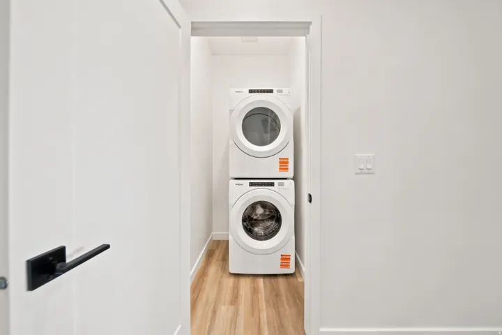 Dedicated laundry closet with stacked appliances and wood-finish flooring