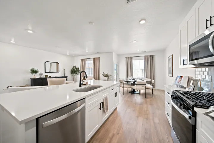 White shaker cabinetry with black hardware, stainless steel appliances, wood-finish flooring, and recessed lighting