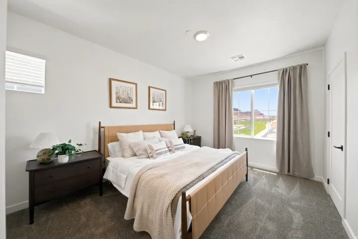 Carpeted flooring, white painted walls, a large window with white trim, and a white interior door with black hardware