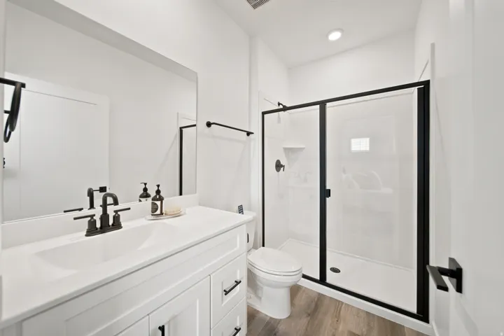 White vanity with integrated sink, black-finish fixtures, frameless wall mirror, and a shower with black-framed glass enclosure