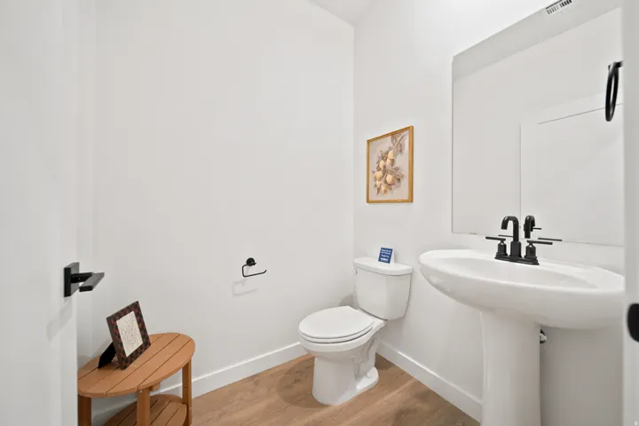 Clean and functional half bath featuring a pedestal sink with matte black faucet, standard toilet, and wood-finish flooring