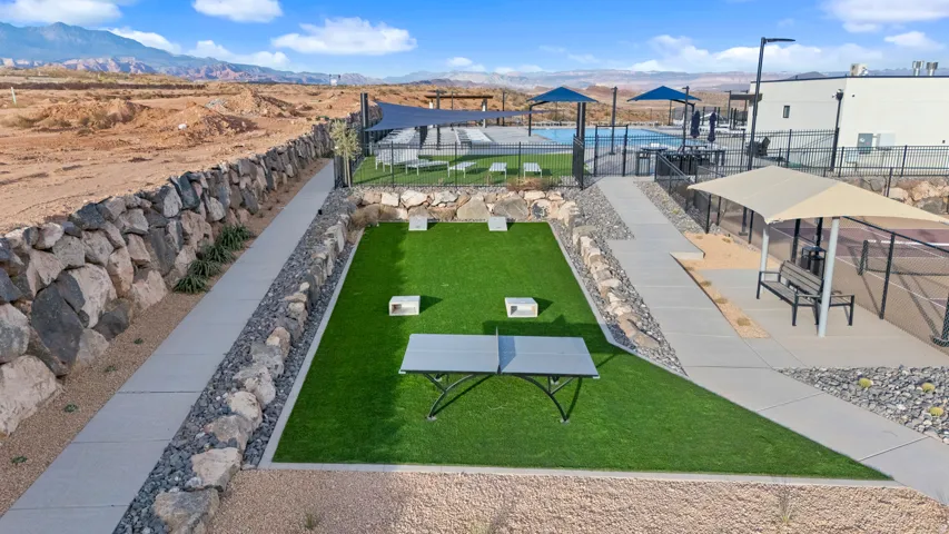 Synthetic turf recreation area with a ping pong table, rock-lined landscaping, concrete pathways, and a stone retaining wall
