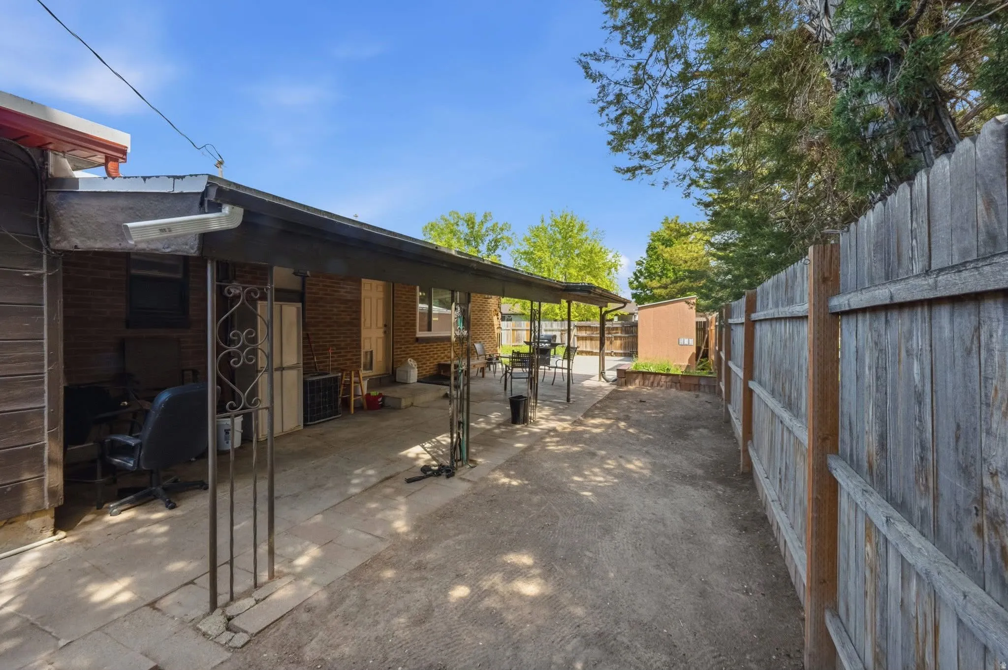 Covered patio area with concrete flooring, brick exterior, wood fence, and mature trees