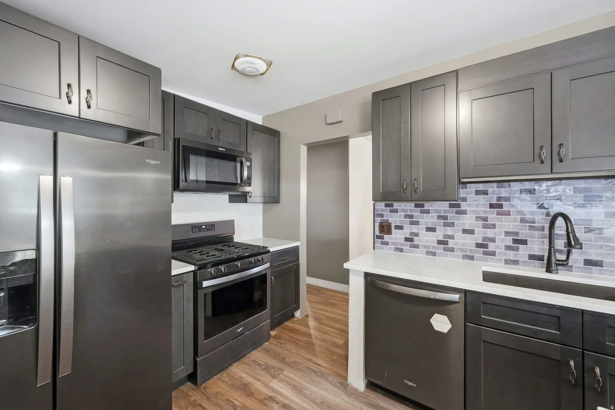 Kitchen featuring wood-finish flooring, dark gray cabinetry, white countertops, and a tiled backsplash