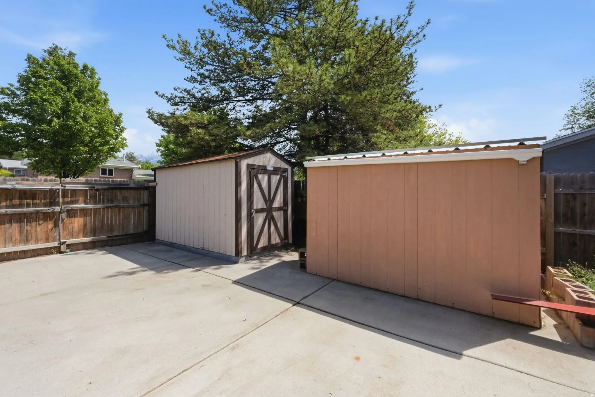 Concrete patio with two storage sheds and a wood privacy fence