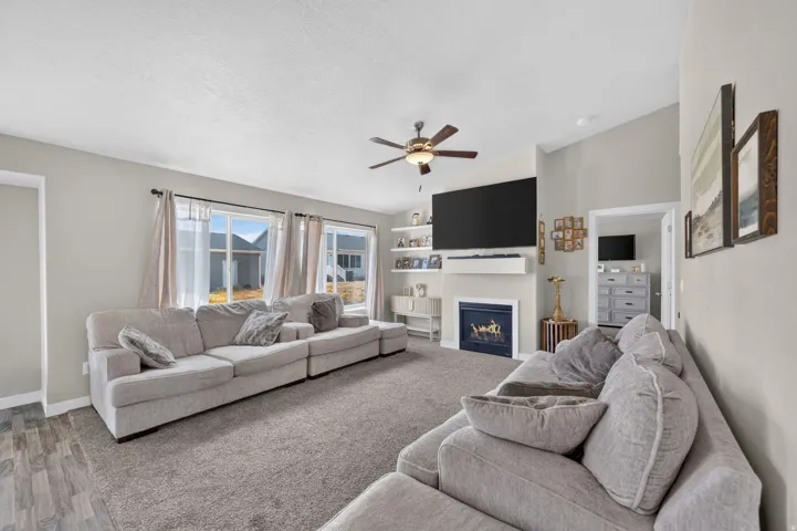 Spacious living area featuring carpet flooring, built-in fireplace with mantel, recessed shelving, and a ceiling fan