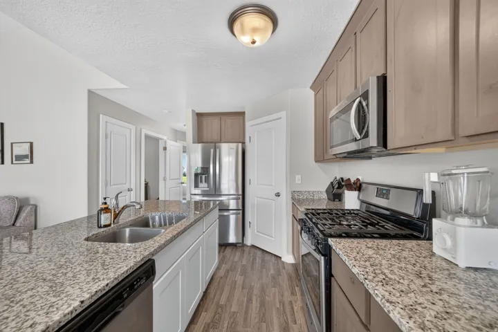 Kitchen featuring wood-finish flooring, stainless steel appliances, granite countertops, an undermount double-basin sink, and recessed lighting