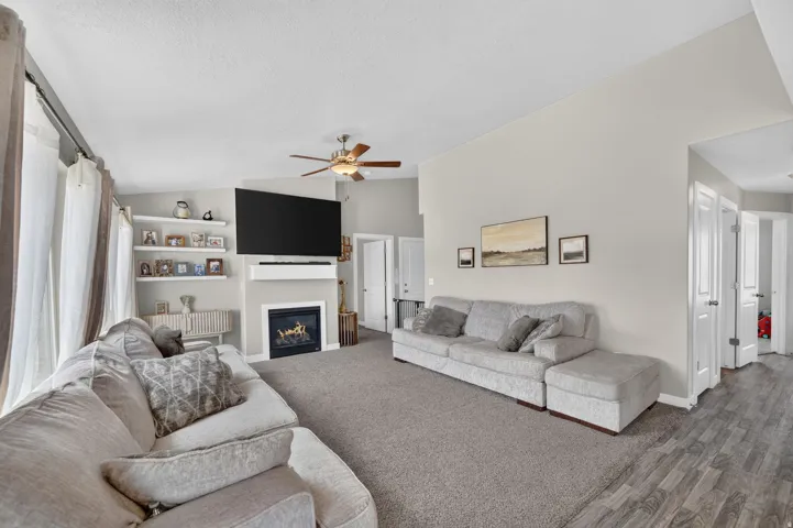 Living area featuring a ceiling fan, a fireplace with a mantel, open shelving, and wood-finish flooring
