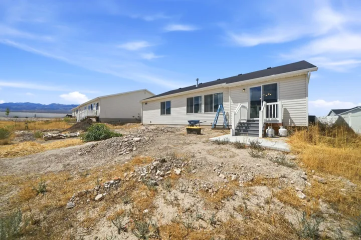 Rear exterior featuring light-colored siding, multiple windows, a sliding glass door, and a small concrete patio