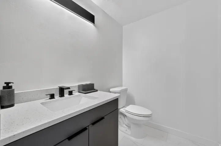 Modern vanity with an integrated rectangular sink, speckled countertop, matte black hardware, and an overhead linear light fixture