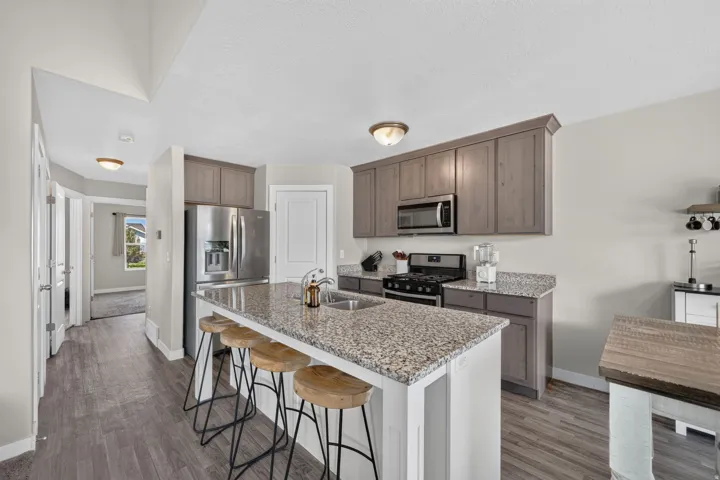 Kitchen featuring light gray cabinetry, stainless steel appliances, a center island with a double basin sink, and granite countertops